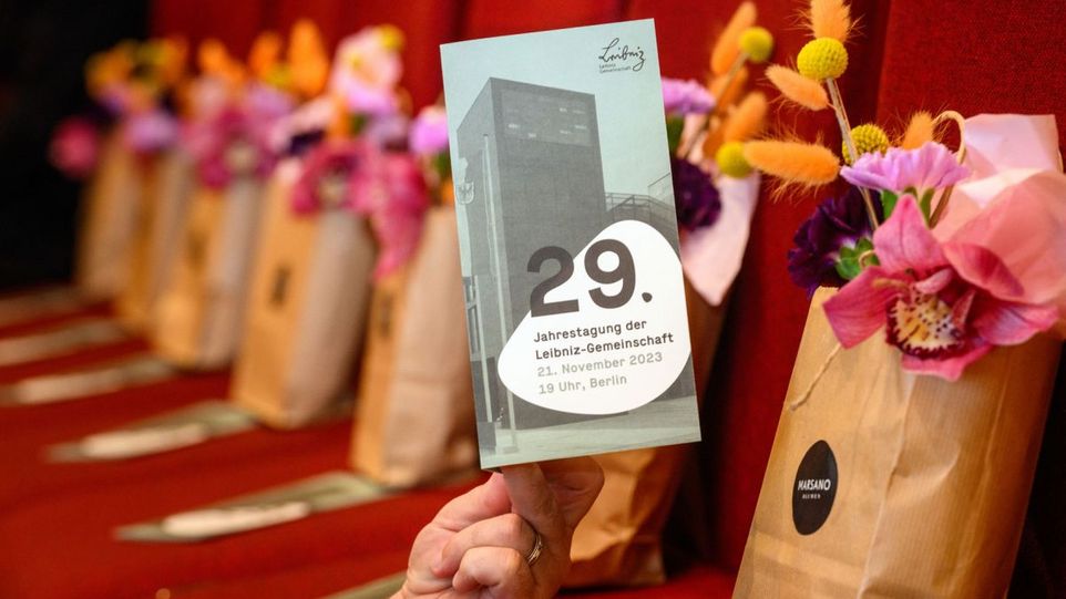 Flyer der Leibniz-Jahrestagung, im Hintergrund Blumensträuße