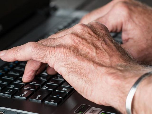Hands of an elderly person typing on laptop 