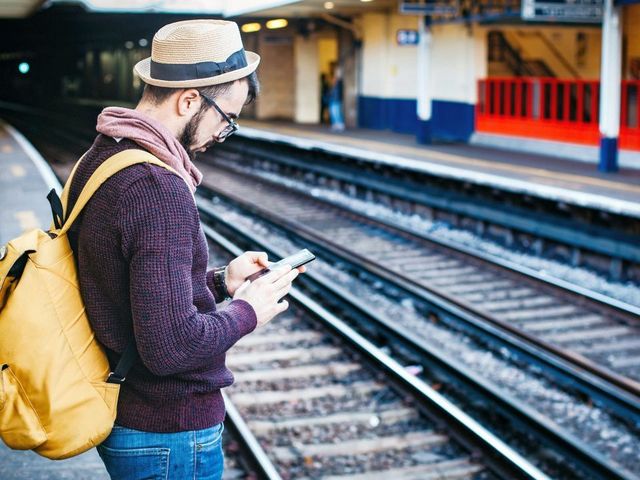 Mann mit Telefon, während er tagsüber vor der Bahnschiene steht