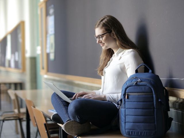 Junge Frau sitzt mit Laptop in Schulflur