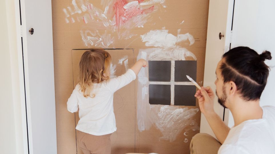 Mann streicht mit seinem Kind unsauber eine Wand