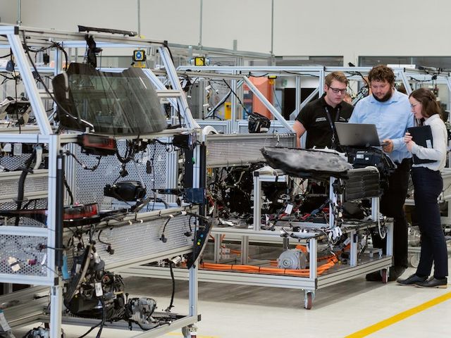 Drei Personen stehen vor einem Laptop in einer Produktionshalle