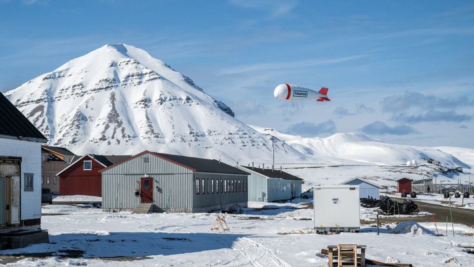 Fesselballon in verschneiter Berglandschaft, im Vordergrund eine Forschungstation