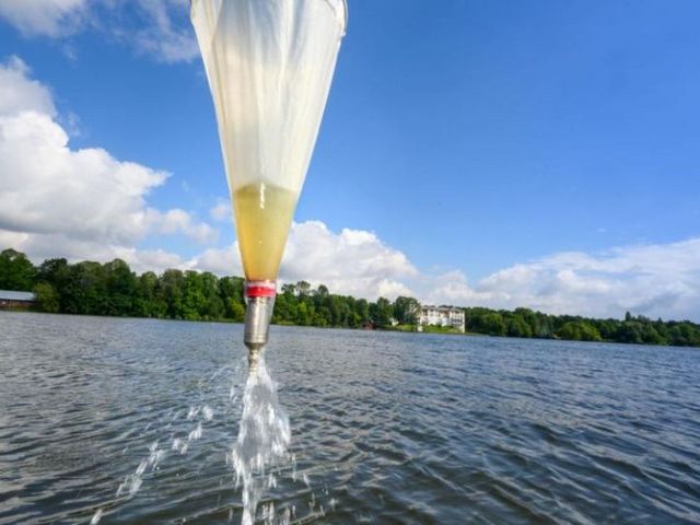 Wasserprobenentnahme auf einem See mit Probenbehälter zur Analyse der Wasserqualität bei sonnigem Wetter