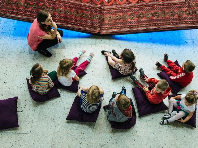 Gruppe von Kindern mit Erzieherin, auf Kissen sitzend