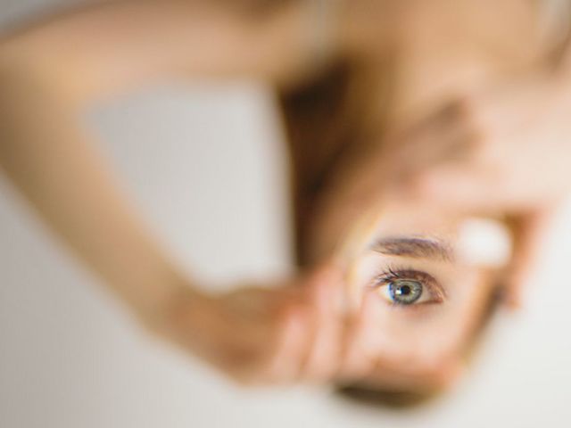 Hände, die einen Spiegel halten, in dem sich das Auge einer Frau spiegelt.