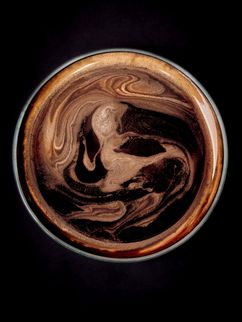 Draufsicht auf eine Tasse Kaffee mit schaumiger Oberfläche und braunen Wirbeln.