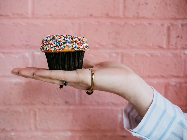 Eine Hand hält einen Muffin mit bunten Streuseln vor einer pinken Wand