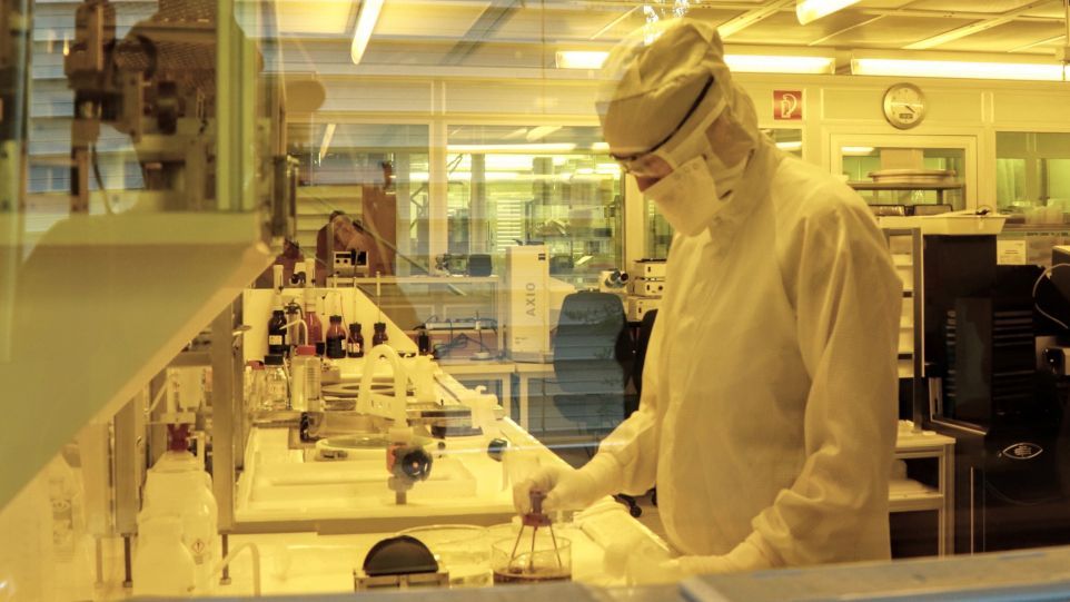 Person mit Sicherheitsanzug und Brille steht im Labor und führt Experiment durch.