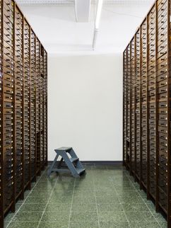 Dunkle Holzschränke zu beiden Seiten mit vielen beschrifteten Schubladen sowie eine kleine Trittleiter. 