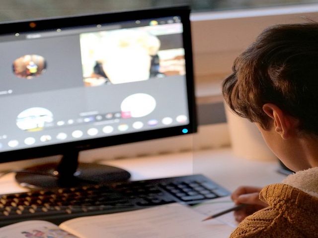 Schüler sitzt vor Bildschirm Zuhause und nimmt an einer Videokonferenz teil 