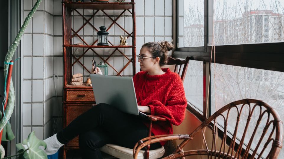 Woman with laptop and mobile phone, sitting at the window of her flat
