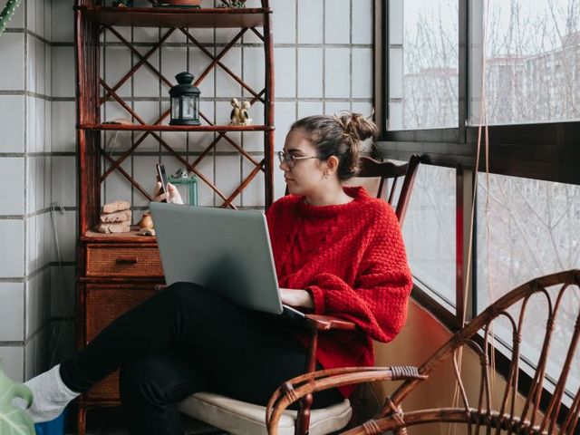 Woman with laptop and mobile phone, sitting at the window of her flat