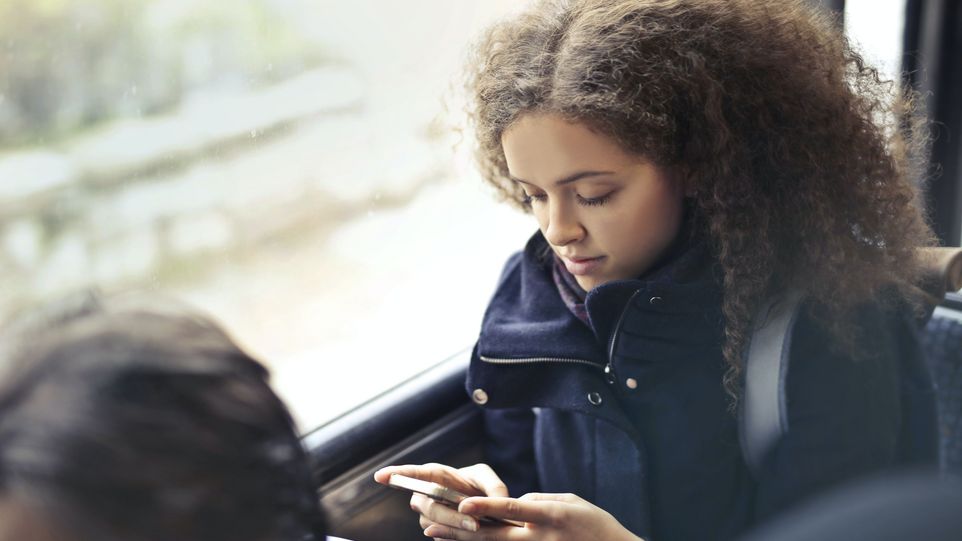 Junge Frau sitzt in öffentlichem Verkehrsmittel mit Blick auf ihr Smartphone.