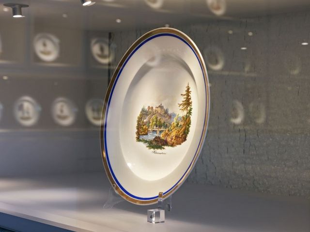 Teller des Herder-Services in einer Vitrine, das Motiv zeigt eine Berglandschaft mit Burg und Fluss