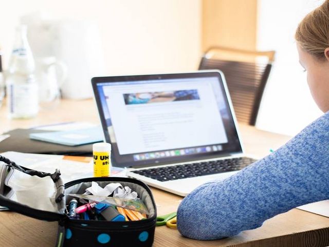 Junges Mädchen arbeitet daheim an einem Laptop, links von ihr befindet sich ein geöffnetes Federmäppchen