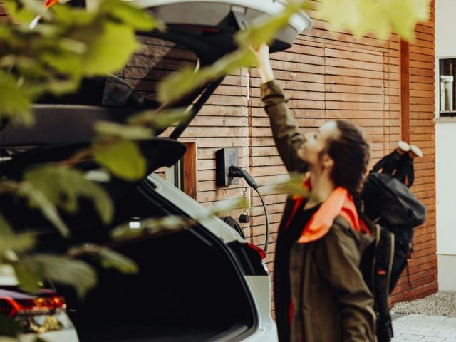 Frau vor Auto, mit elektrischer Ladesäule im Hintergrund