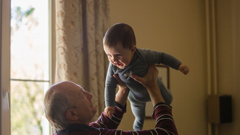 Elderly man holds toddler in the air