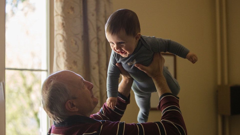 Elderly man stretches child in the air