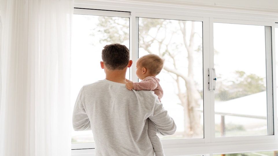 Vater mit Kleinkind auf dem Arm, aus dem Fenster schauend