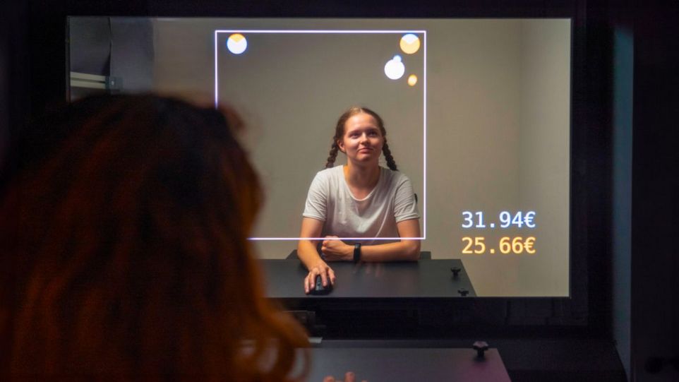 Dyadische Interaktionsplattform, auf der zwei Teilnehmende das Kooperations-Wettbewerbs-Spiel spielen. Transparenter Bildschirm zwischen zwei Personen mit Markierungen und Euro-Summen