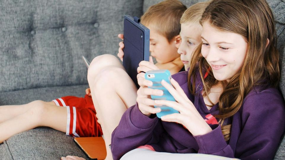 Drei Kinder mit Smartphones und Tablets auf einer Couch