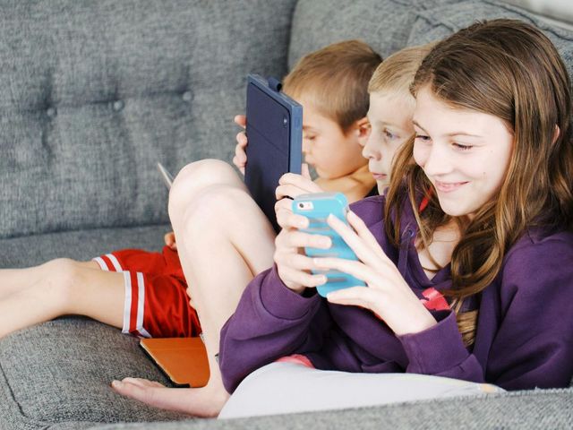 Drei Kinder mit Smartphones und Tablets auf einer Couch 