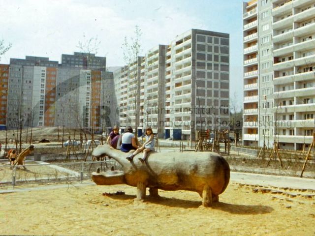 Ein Spielplatz mit Kindern auf einem Holzflusspferd, umringt von Plattenbauten