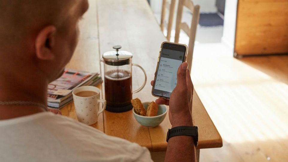 Mann am Frühstückstisch schaut auf sein Handy mit Blutzucker-Messdaten