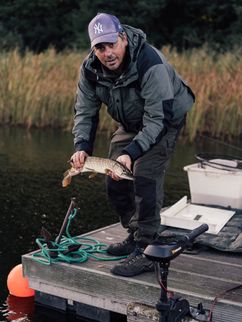 Robert Arlinghaus hält einen gefangenen Fisch auf einem Holzsteg über dem Wasser.