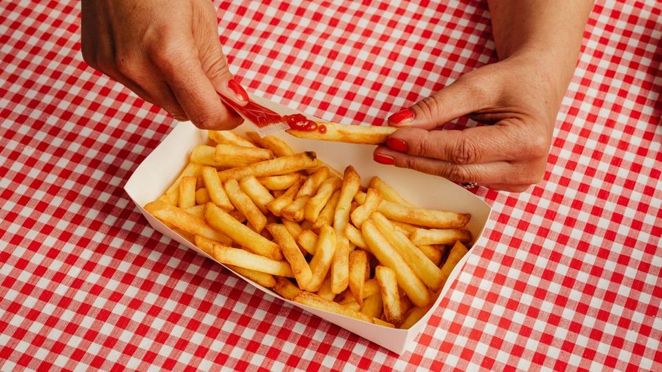 Hand, die Ketchup auf Pommes verteilt