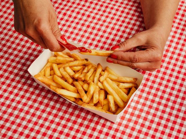 Hand, die Ketchup auf Pommes verteilt