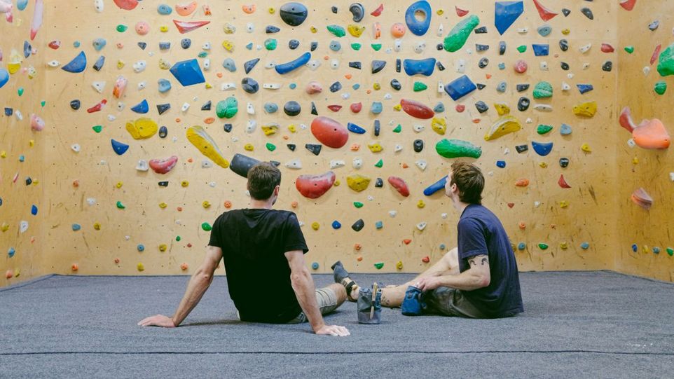 Zwei Männer sitzen vor einer Boulderwand und ruhen sich aus