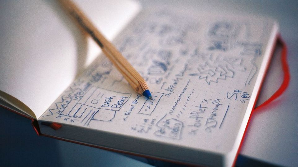 Opened notebook with drawn designs, on it a pencil
