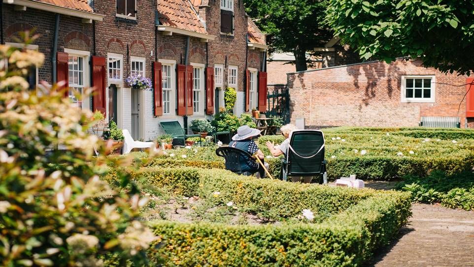 Row houses with well-kept front gardens, in one of them two elderly ladies are sitting and talking.