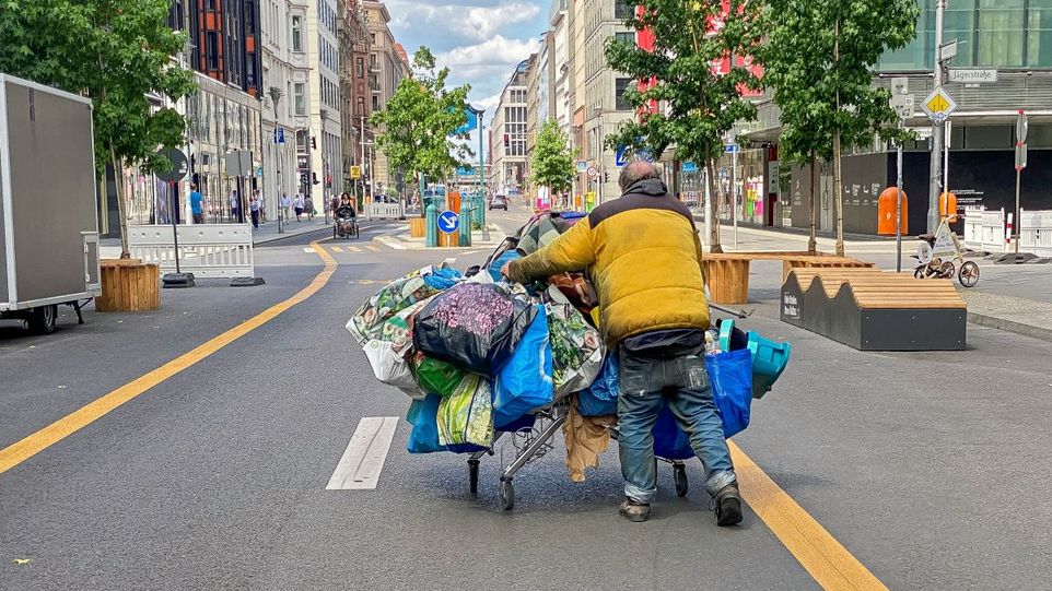 Mann schiebt sein Hab und Gut in einem Einkaufswagen voller Plastiktüten durch eine Geschäftsstraße