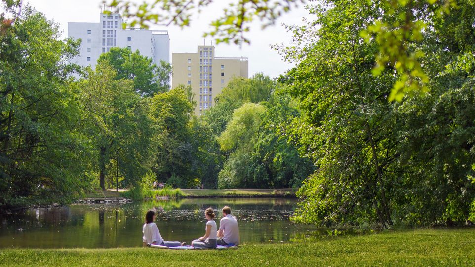 Three people sit by the lake in the park.