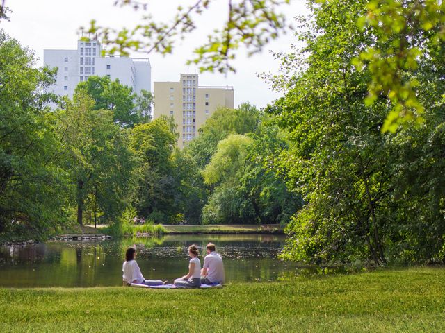 Three people sit by the lake in the park.