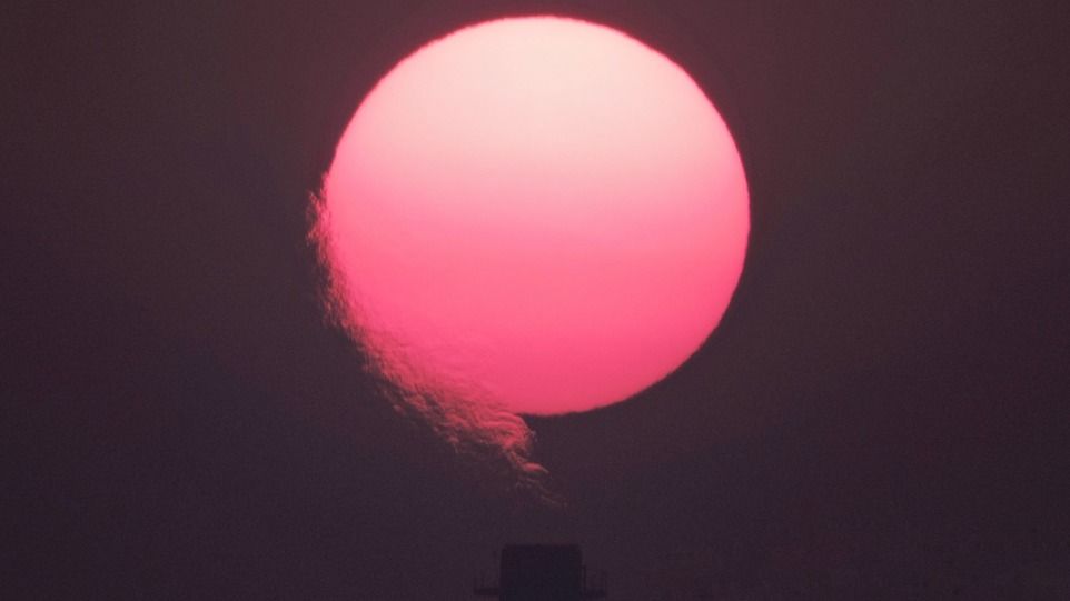 Rötliche Sonne mit Rauch aus Schornstein im Vordergrund