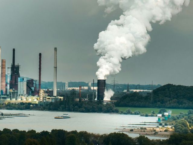 Industrieanlage mit rauchenden Schornsteinen am Flussufer
