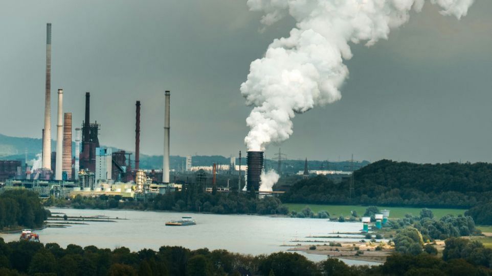 Industrieanlage mit rauchenden Schornsteinen am Flussufer