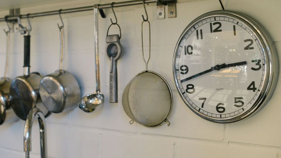 Wanduhr neben Töpfen und Küchengerät
