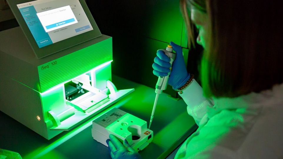 Wissenschaftlerin mit Pipette vor Genomsequenzierungs-Apparat